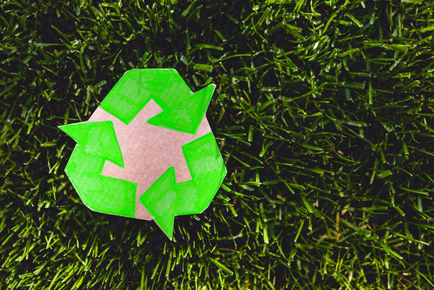 recycle sign hand drawn on cardboard resting on perfect green grass from private lawn, shot under strong sunlight - 写真・画像