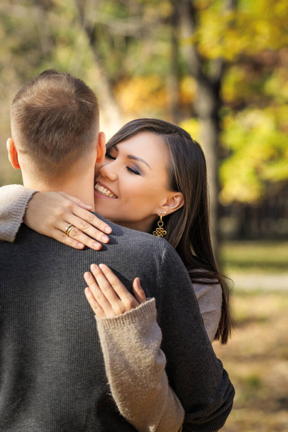 Beautiful young woman lovingly hugging her man in autumn park, vertical. - Foto, Bild