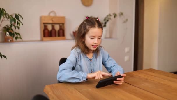 Щаслива дівчинка грає в гру на мобільному телефоні вдома, дитина використовує смартфон, залежність від смартфона, емоційна дівчина
. - Кадри, відео