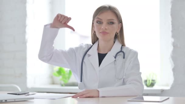 Médico femenino mostrando pulgares hacia abajo mientras está sentado en la clínica - Imágenes, Vídeo