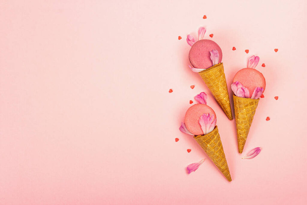 Ice cream waffle cones with macarons on pink background. Sweet dessert, colorful and pastel candy colors, summer concept. Romantic style, festive card, top view - 写真・画像