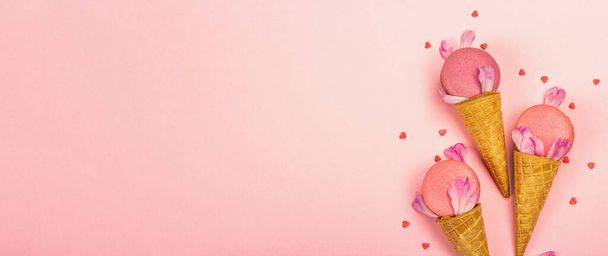 Zmrzlinové vafle kornouty s makarony na růžovém pozadí. Sladký dezert, barevné a pastelové sladkosti, letní koncept. Romantický styl, slavnostní přání, banner formát - Fotografie, Obrázek
