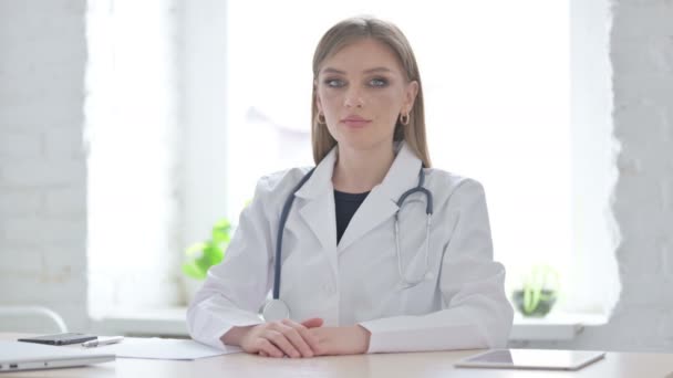 Médico femenino mirando la cámara mientras está sentado en la clínica - Imágenes, Vídeo