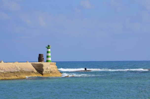Middellandse Zee. Haven van Jaffa in Israël. Groene vuurtoren, golven die tegen de steen botsen. Onderwerp: reizen, vakantie op zee, zeilen, zeilen. Plaats voor tekst - Foto, afbeelding