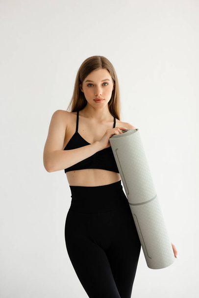 Sports girl holding a fitness mat in her hands on a white background. High quality photo - Photo, Image