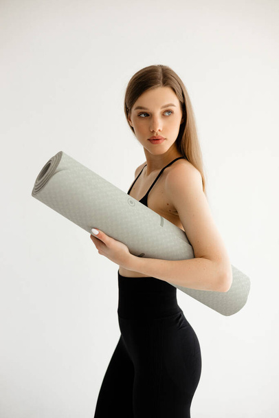Ragazza sportiva in possesso di un tappeto fitness tra le mani su uno sfondo bianco. Foto di alta qualità - Foto, immagini