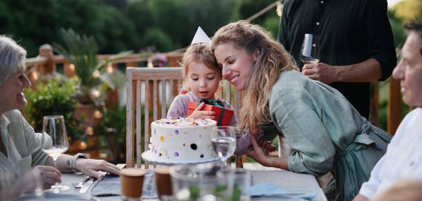 A multi generation family celebratiing birthday of little girl and having garden party outside on patio. - Φωτογραφία, εικόνα