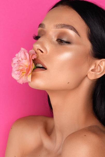 eine schöne brünette Frau Porträt, eine rosa Blume im Mund, rosa Hintergrund - Foto, Bild