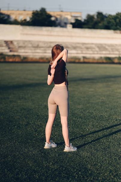 Athletic Girl Clasps Her Hands in Castle Behind Her Back. Gymnastic Exercise for Back. Do workout in nature. To breathe fresh air. - Foto, imagen