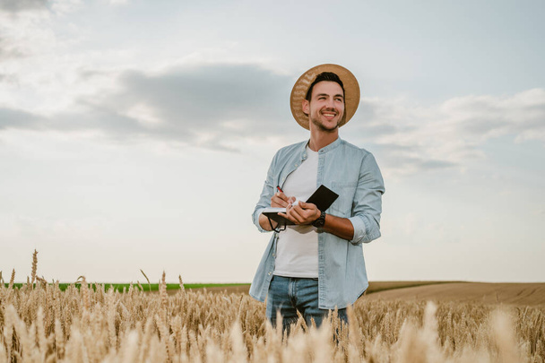 Happy farmer  writing notes  while standing in his growing  wheat  field. - 写真・画像