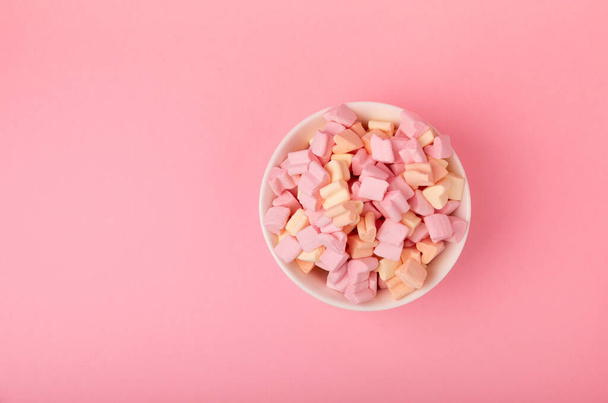 Marshmallows in a ceramic bowl on a pink background. Chewing candy with strawberry flavor close-up. Snacks and snacks for parties. Spice for coffee and cocoa. Winter food concept. Space for text.  - Foto, immagini