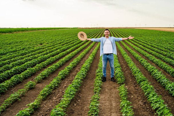 Gelukkige boer met uitgestrekte armen in zijn groeiende soja veld. - Foto, afbeelding