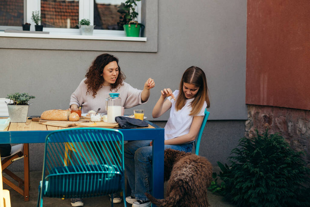 mother and daughter feeding their dog while having breakfast in backyard - Фото, изображение