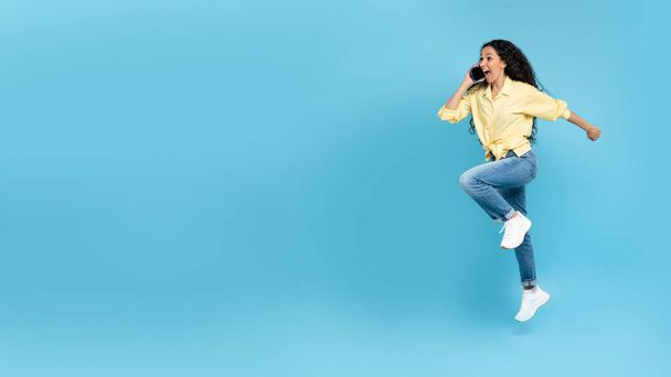 Aufgeregte junge Frau telefoniert, telefoniert, springt und rennt auf gelbem Hintergrund, Panorama mit Leerstelle. Coole Millennial-Frau beim Telefonat. Moderne Kommunikation - Foto, Bild