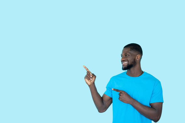 Demonstrating man. Presentation advertising. Special offer. Recommending cheerful guy pointing at invisible product on blue copy space background. - Zdjęcie, obraz