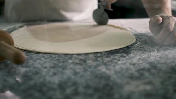 Der Koch schneidet die Ränder des runden Teigs mit einer speziellen Rolle ab. Blick hinter Glas. Hochwertiges 4k Filmmaterial - Filmmaterial, Video