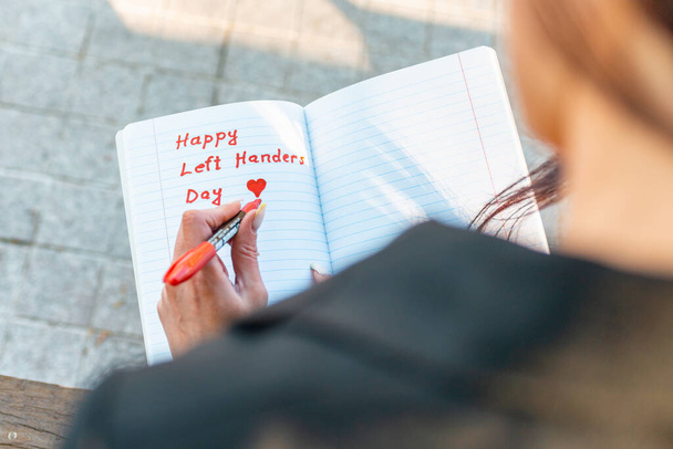 Vrouw schrijft in een notitieboekje, houdt viltstift in haar linkerhand.Buiten zomeravond park. Linkshandigen Dag 13 augustus. Close-up. - Foto, afbeelding