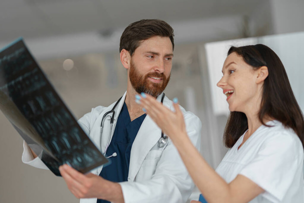 Due medici in uniforme guardano e discutono una radiografia o una risonanza magnetica della colonna vertebrale del paziente in clinica - Foto, immagini