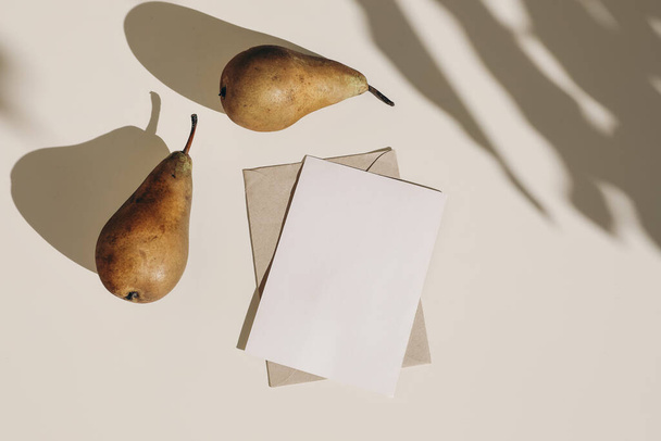 Summer still life composition. Autumn weddding greeting card, envelope mock up scene. Two pears fruit, long harsh shadows overlay. Beige table background in sunlight, flat lay, top view, no people. - Fotografie, Obrázek