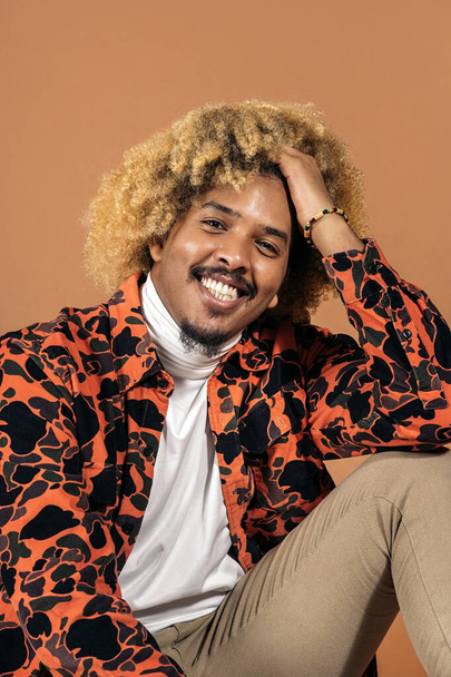 Stock photo of cheerful afro man smiling and looking at camera in studio shot against brown background. - Φωτογραφία, εικόνα
