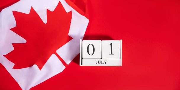 Concept de la fête du Canada avec fragment de drapeau canadien et date du 1er juillet sur calendrier en bois blanc sur fond rouge vif, bannière plate - Photo, image