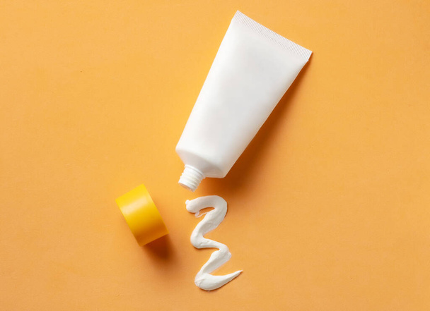 Mockup of White cosmetic tube with sunscreen cream and squeezed cream texture on orange background. Top view - Fotó, kép