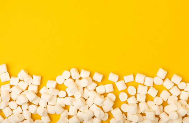 Loose marshmallows on a yellow background. White marshmallow flat lay. Sweets and snacks for a snack. Chewing candies close-up. Copy space. Place for text. Winter food concept. - 写真・画像