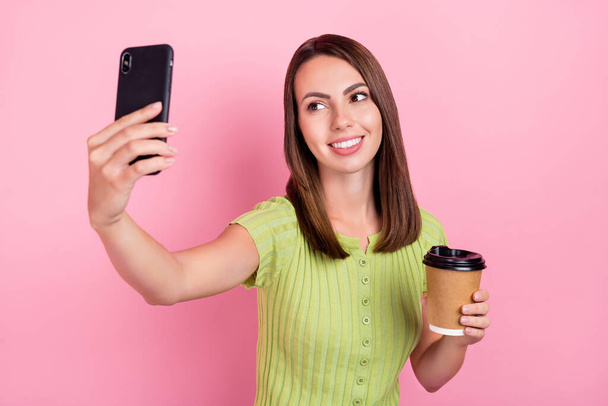 Photo de douce brune jeune femme boire du café faire selfie porter t-shirt vert isolé sur fond de couleur rose. - Photo, image
