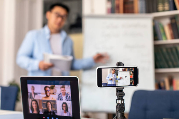 Elektronikus tanulás. Felismerhetetlen ázsiai tanár férfi tanítás Csoportos videohívás távolsági hallgatókkal telefonnal és laptoppal. Online osztály, Internet és oktatás. Sekély mélység - Fotó, kép