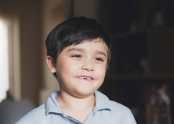Κινηματογραφικό Πορτρέτο Παιδί που φαίνεται βαθιά στη σκέψη, Δραματικό χαρούμενο Νεαρό αγόρι που κοιτάζει έξω με χαμογελαστό πρόσωπο. Ένα παιδί παίζει μόνο στο σαλόνι το βράδυ. - Φωτογραφία, εικόνα
