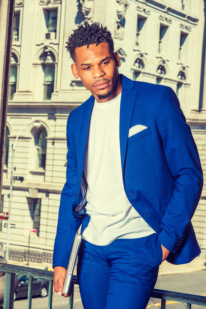 ニューヨークで働くアフリカ系アメリカ人ビジネスマン。青のスーツを着て白いTシャツを着てノートパソコンを持って黒の大学生キャンパスのヴィンテージの建物のそばに立って - 写真・画像