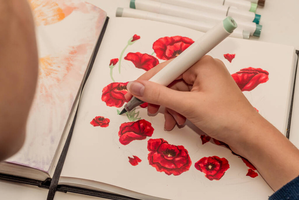 Hand drawing a red poppy wreath sketch in a sketchbook with alcohol based sketch drawing markers. Remembrance Day and Anzac day. - Foto, Imagen