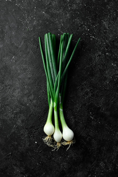 Fresh green onions on a black stone background. Healthy food. Top view. - Foto, imagen