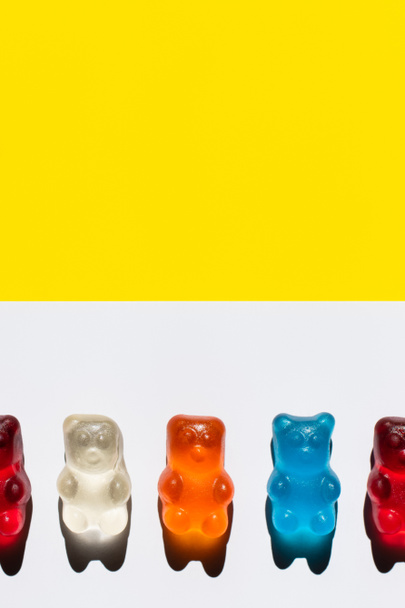 Close up view of colorful jelly bears on white and yellow surface - Photo, Image