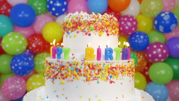 Pastel con velas de cumpleaños con globos multicolores sobre fondo. - Metraje, vídeo