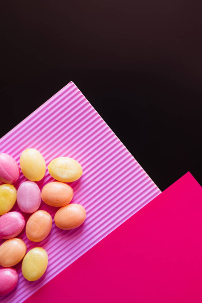 Вид сверху цветных конфет на розовой поверхности, изолированной на черной  - Фото, изображение