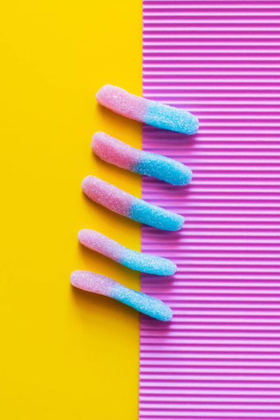 Colocación plana con dulces de gelatina de colores sobre fondo rosa y amarillo  - Foto, Imagen