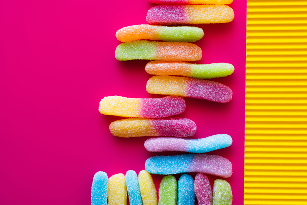 Flache Lage bunter Gelee-Bonbons auf rosa und texturierter gelber Oberfläche  - Foto, Bild