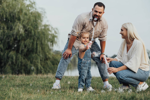 Portrait of Happy Young Family, Mom and Dad with Their Little Daughter Having Fun Outdoors Outside City - Foto, afbeelding