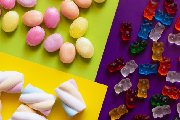 Colocación plana de malvaviscos cerca de caramelos y osos de gelatina en una superficie colorida  - Foto, imagen