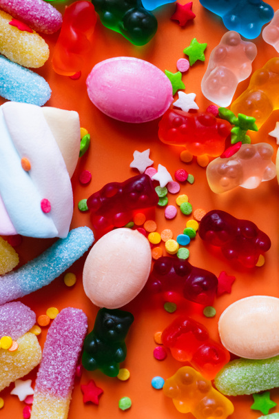 Nahaufnahme von bunten Süßigkeiten und Zuckerguss-Dekor auf orangefarbenem Hintergrund  - Foto, Bild
