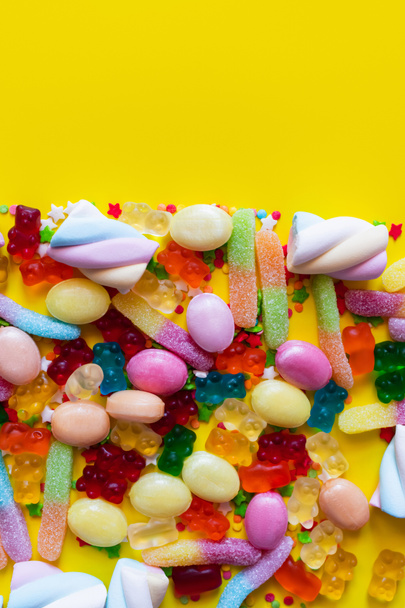Top view of fluffy marshmallows and jelly sweets on yellow surface  - Фото, зображення