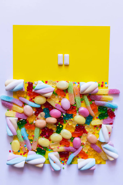 Вид зверху жувальних ясен біля барвистих цукерок на білій і жовтій поверхні
  - Фото, зображення