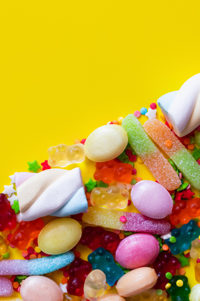 Επίπεδη lay με πολύχρωμα γλυκά ζελέ και νόστιμα marshmallows σε κίτρινο φόντο  - Φωτογραφία, εικόνα