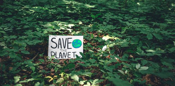 Plakat mit der Aufschrift Rettet den Planeten im Wald unter Pflanzen, das Konzept der Ökologie, die Liebe zur Natur. - Foto, Bild