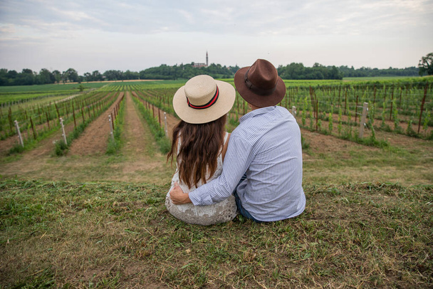 Una pareja sentada en el suelo se abrazan mientras miran los viñedos, un apasionado momento de amor - Foto, Imagen