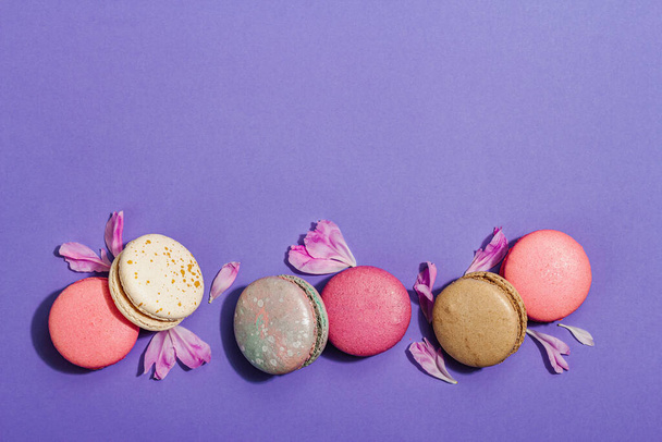 Macarons met pioenrozen bloemblaadjes op zeer peri kleur achtergrond. Zoet dessert, kleurrijke en pastel snoep kleuren, zomer concept. Romantische stijl, feestelijke kaart, flat lay, bovenaanzicht - Foto, afbeelding