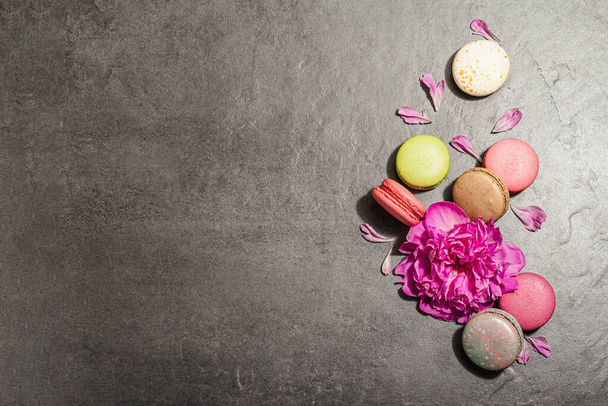 Macarons con fiore di peonia su uno sfondo di pietra. Dolce dessert, colori colorati e pastello. Stile romantico, biglietto da visita, posa piatta, luce dura, ombra scura, vista dall'alto - Foto, immagini