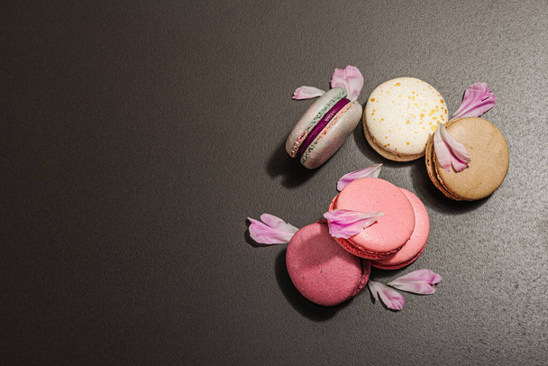 Macarons with peony flower on a black stone background. Sweet dessert, colorful and pastel colors. Romantic style, festive card, flat lay, hard light, dark shadow, top view - Foto, Bild