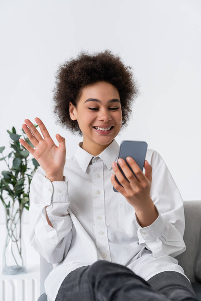 スマートフォンでのビデオ通話中に手を振っている陽気なアフリカ系アメリカ人女性  - 写真・画像